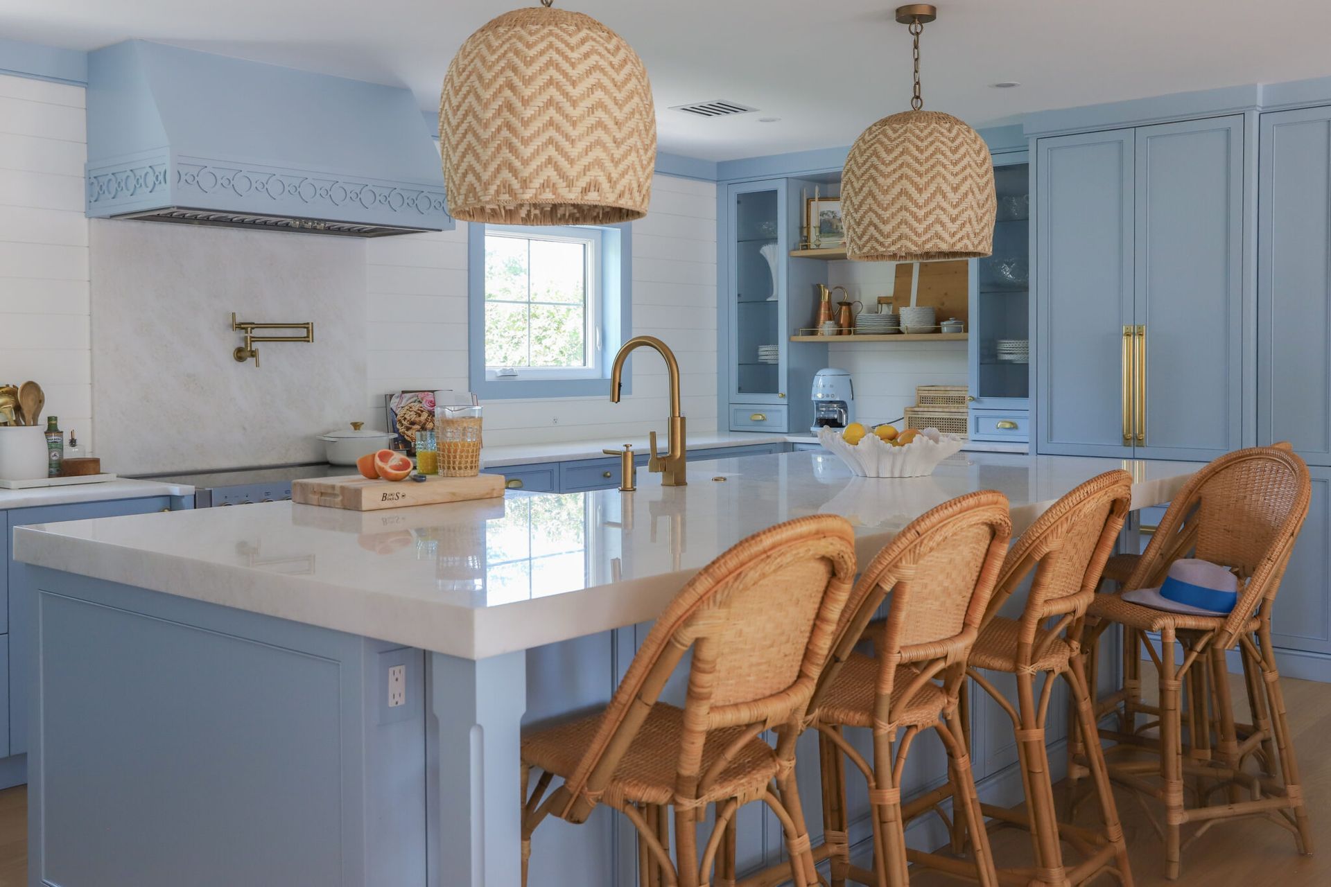 Coastal kitchen with blue cabinets, white countertops, woven pendant lights, and rattan bar stools.