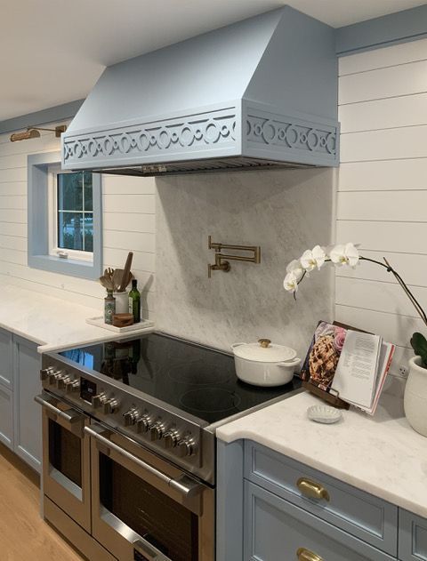 Light blue kitchen with a range, hood, and marble backsplash.