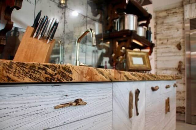 Rustic kitchen with weathered wood countertop and cabinets, gold faucet, and unique driftwood handles.