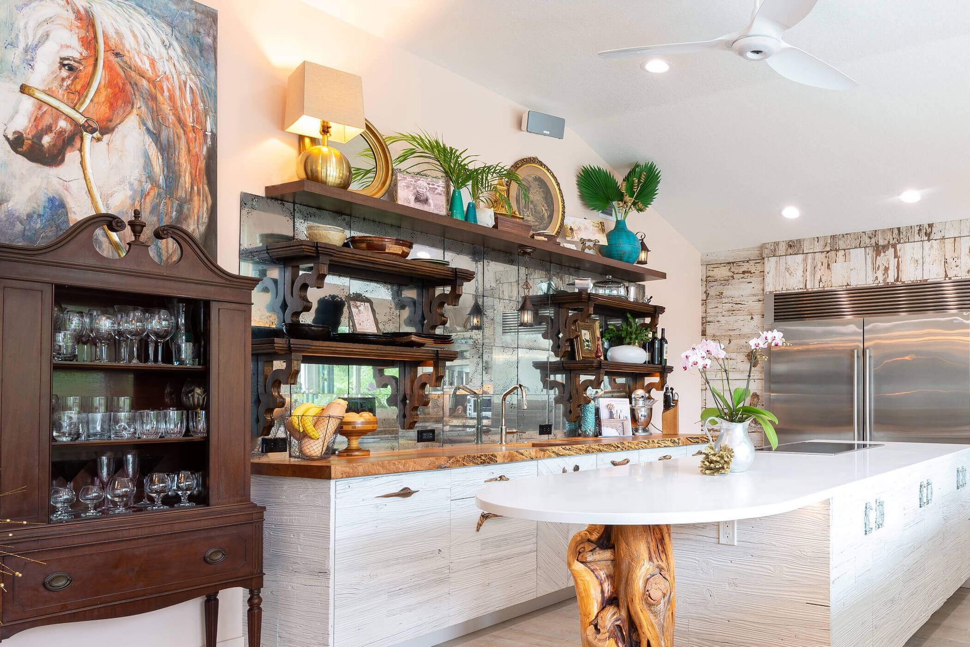 Kitchen with wood shelves, cabinets, and a white island. A horse painting and glass display cabinet are visible.