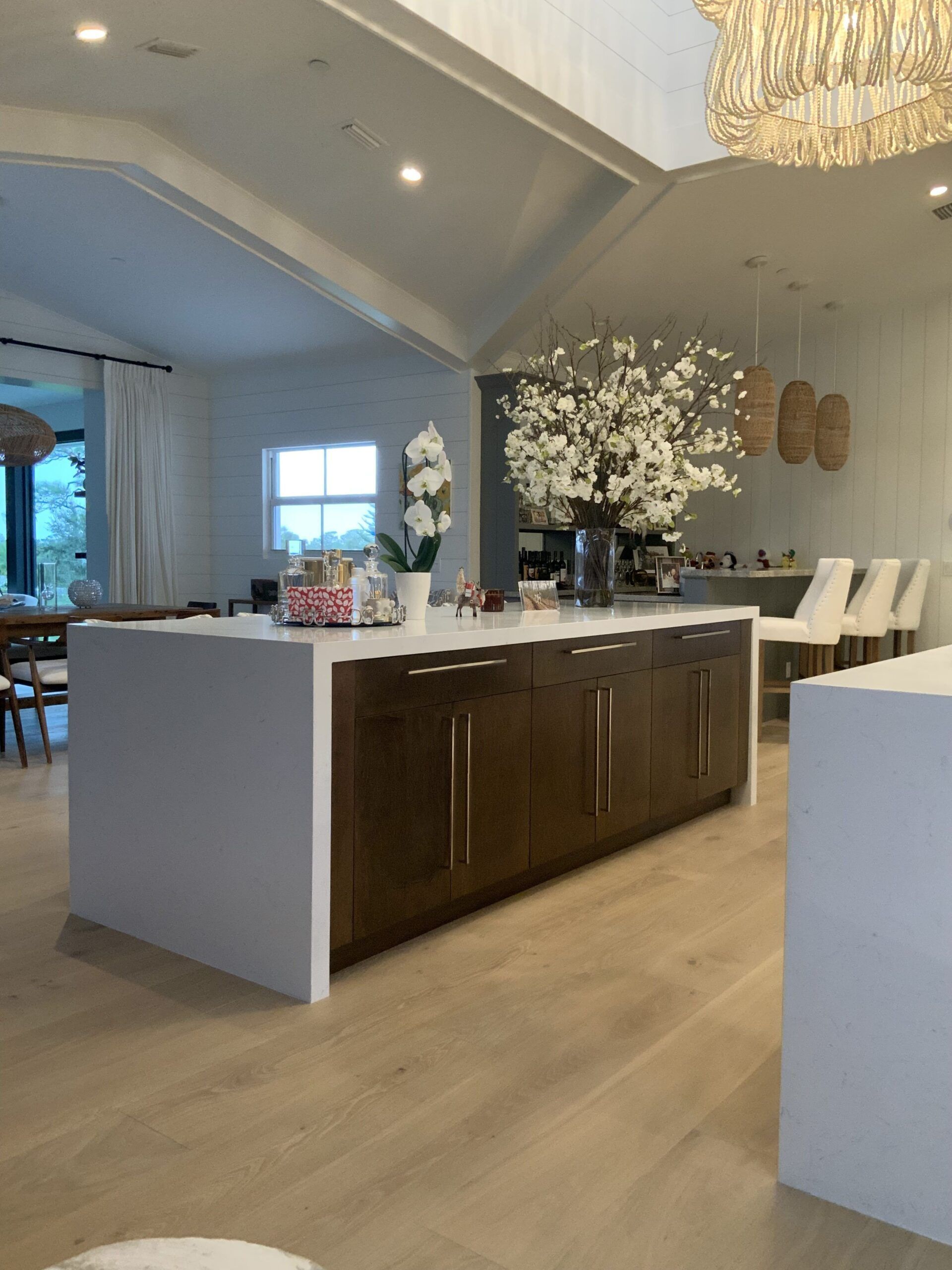 Large kitchen with dark wood island, white countertops, and floral arrangement. Bright, open space.