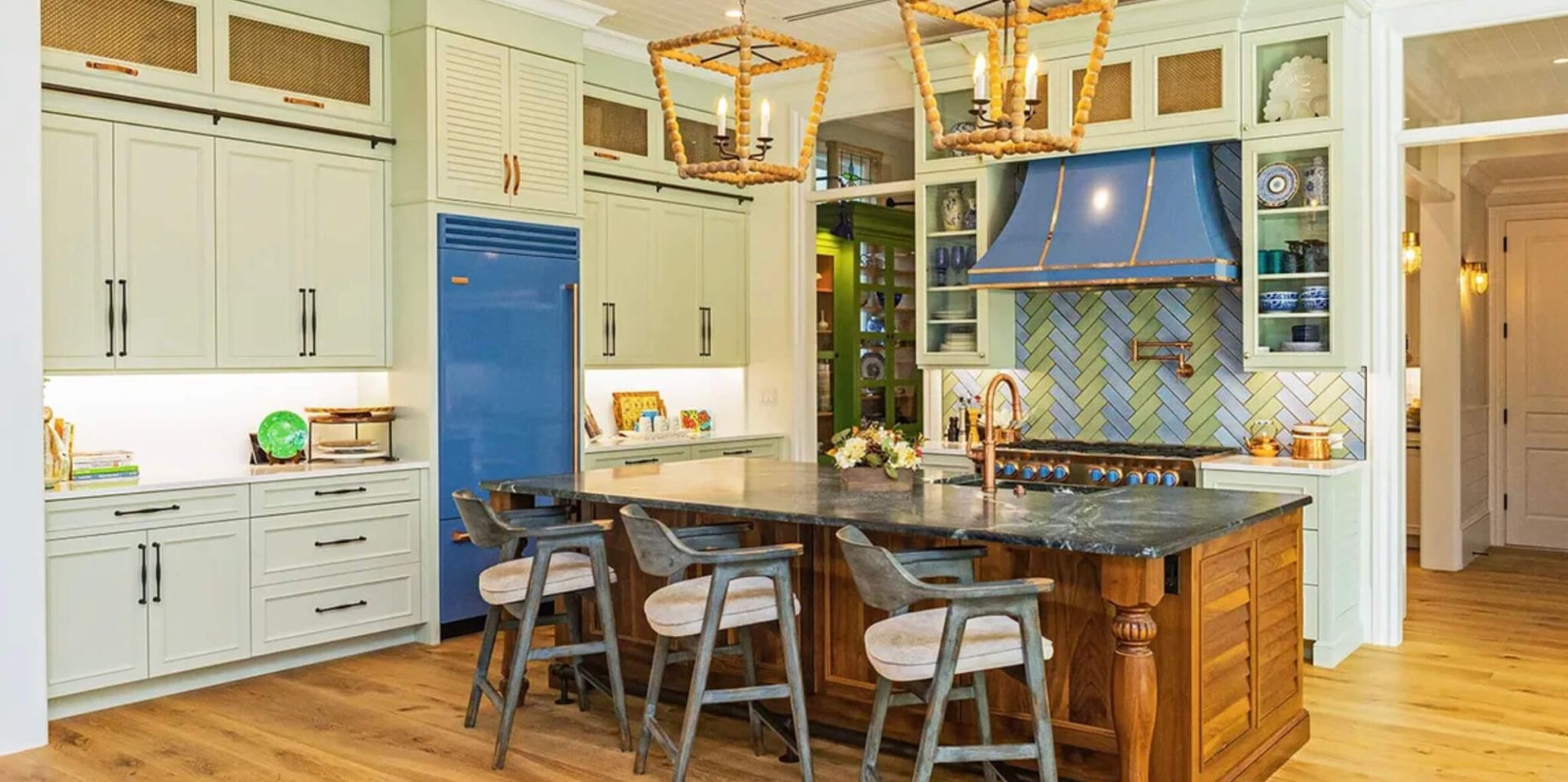 A spacious kitchen with a blue refrigerator, wooden island, and two golden hanging lights.