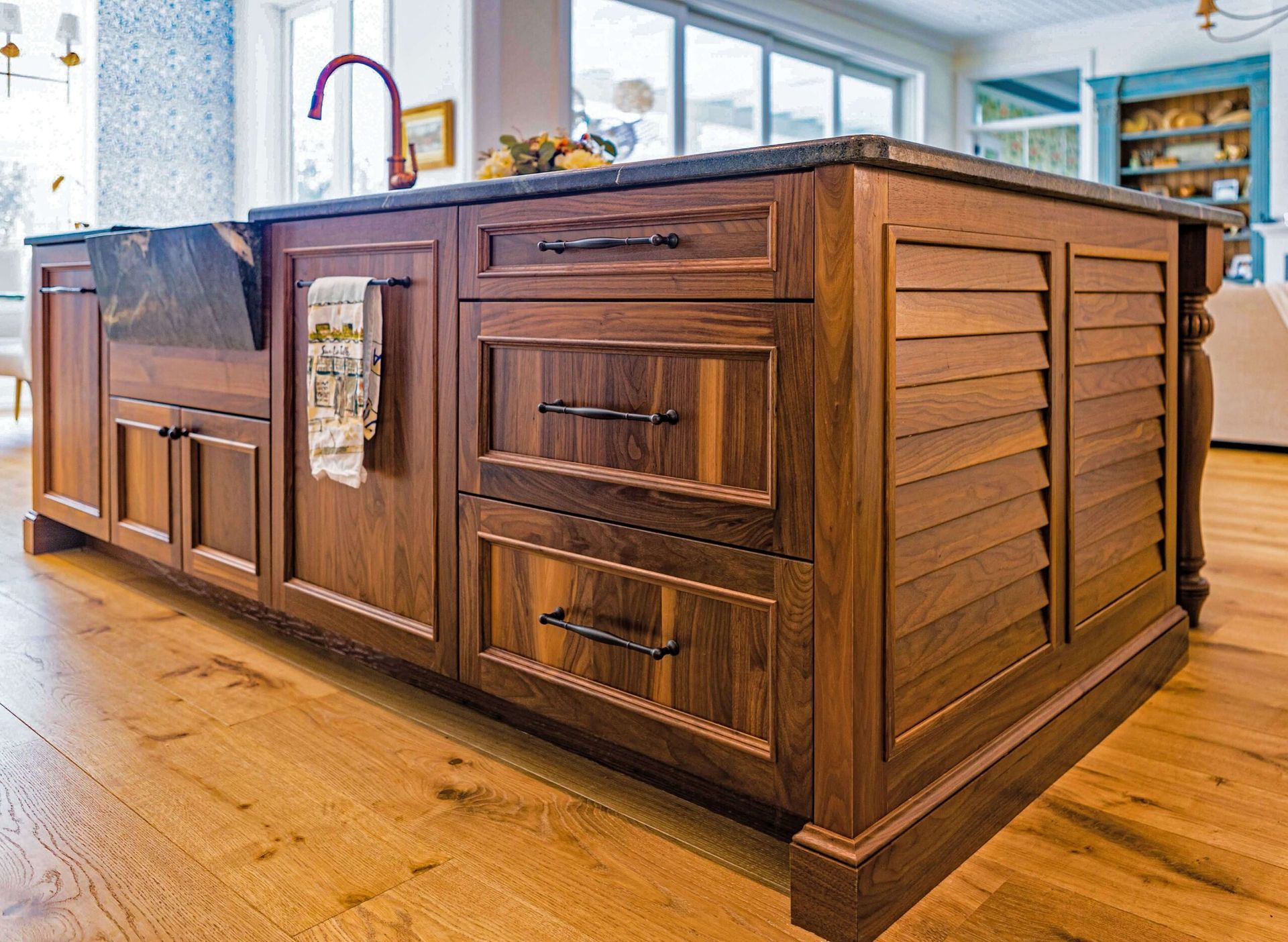 Wooden kitchen island with dark countertop, sink, drawers, and shutter-style side panels.
