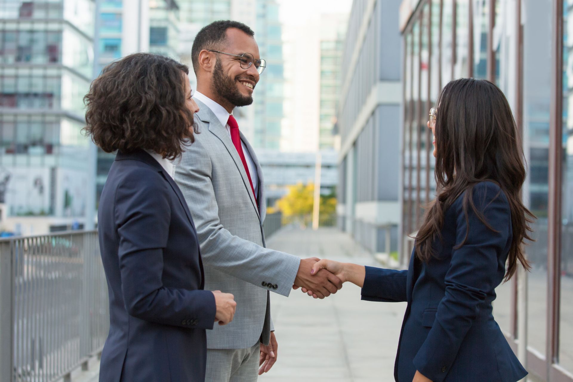 Three business professionals shaking hands outside an office building