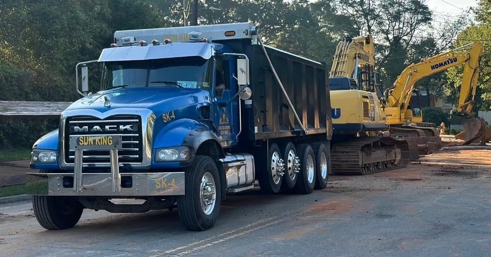 A blue mack dump truck is parked next to a yellow excavator