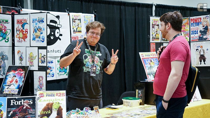 A man with a beard is sitting at a table at a convention.