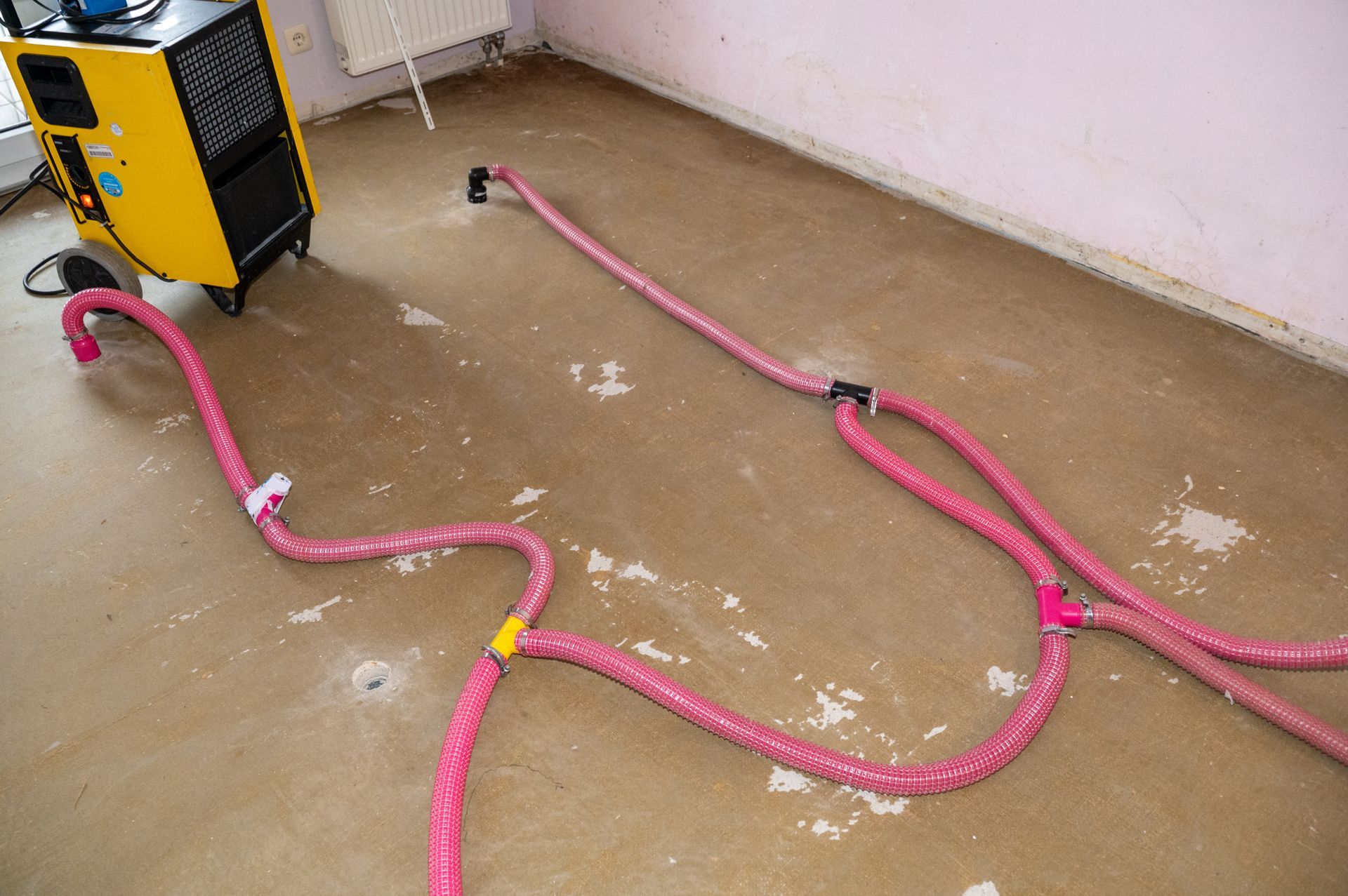 Water extraction hoses connected to industrial drying equipment on a flooded interior floor. Water extraction hoses connected to industrial drying equipment on a flooded interior floor.