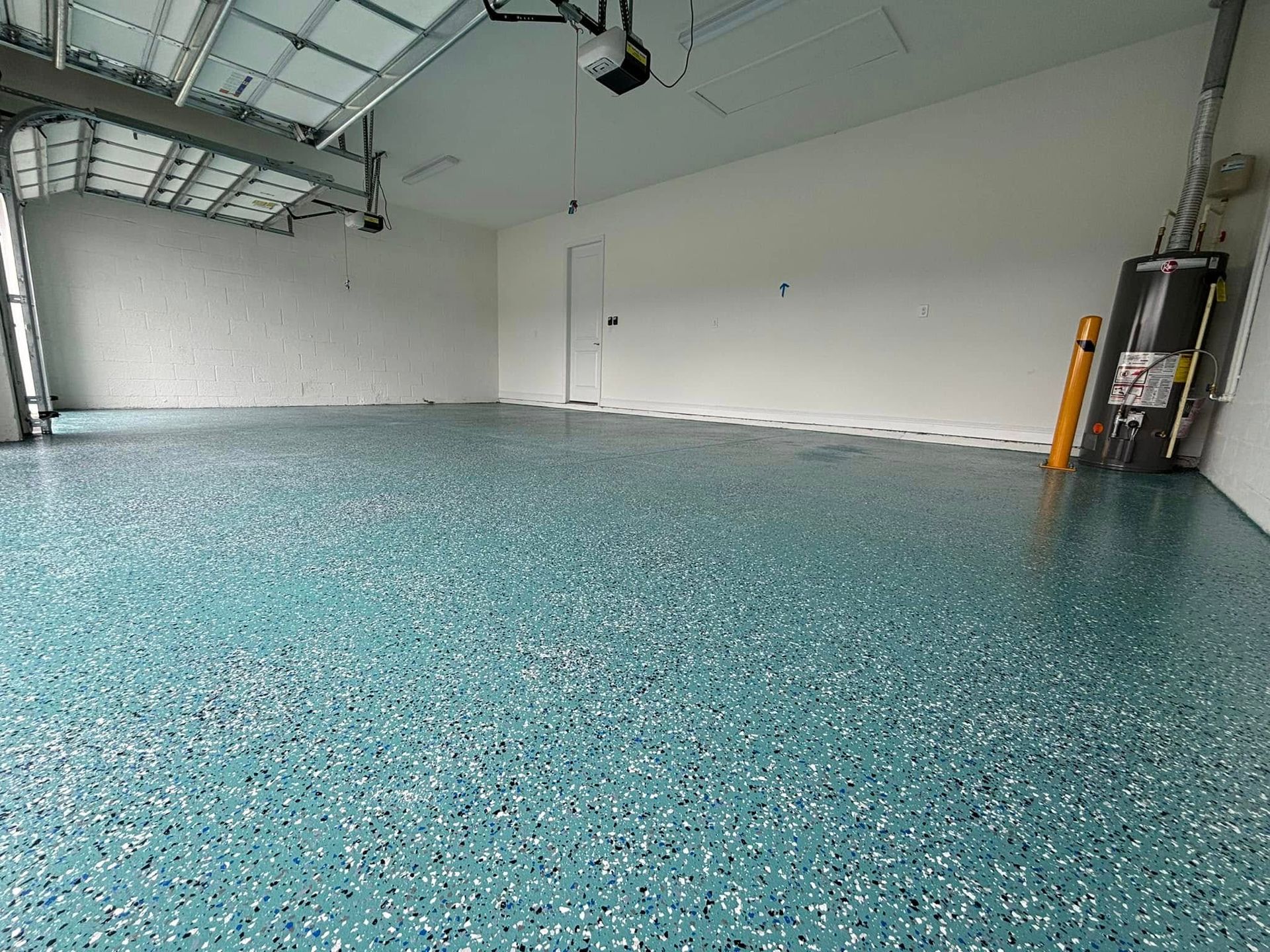 Spacious garage with epoxy floor.  Blue, white and black speckled flooring, white walls, open garage door.