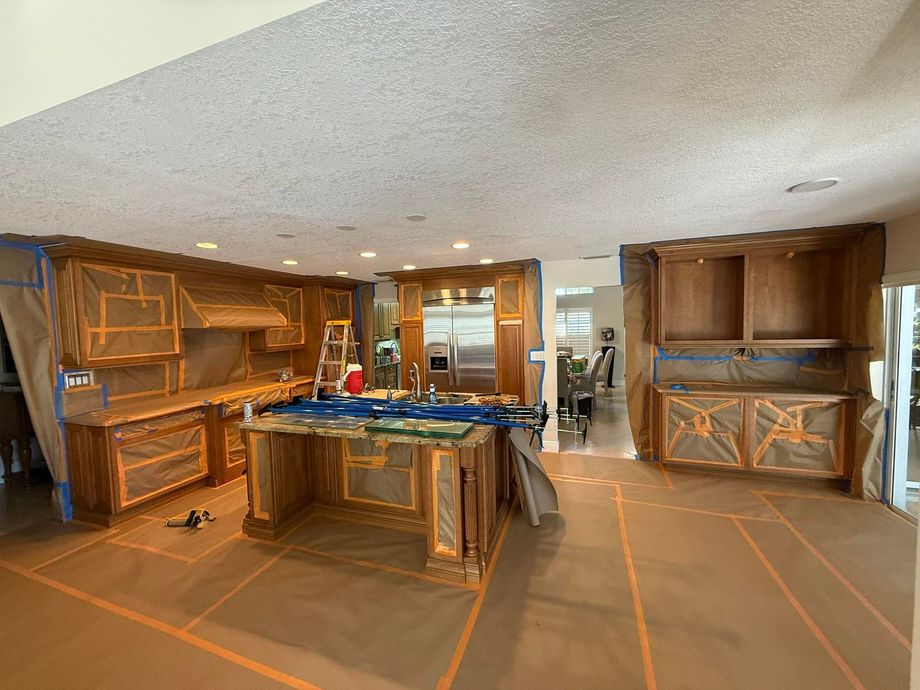 Kitchen with cabinets covered in brown paper for painting, with a ladder and supplies on the island.