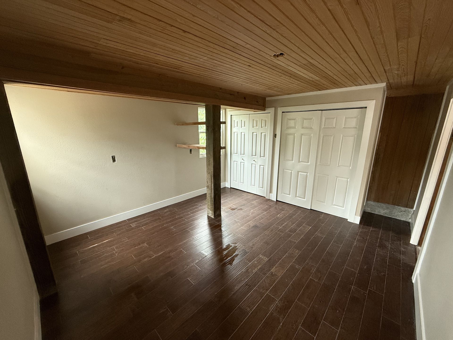 Empty room with wood floors and ceiling, white doors, and a support beam.
