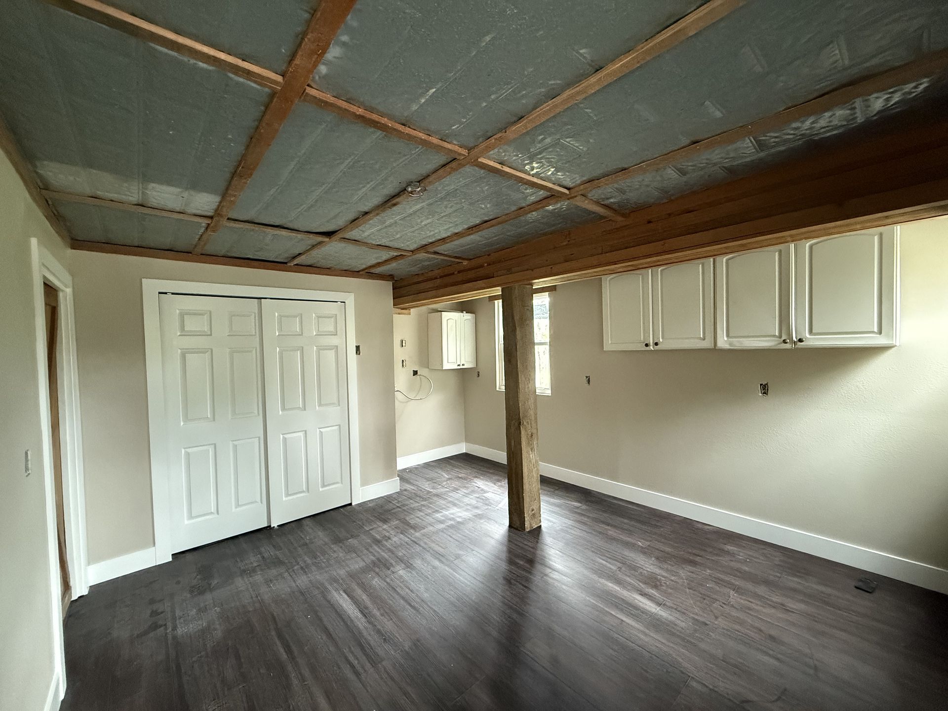 Interior room with dark wood floor, white walls, cabinetry, and wooden ceiling beams.