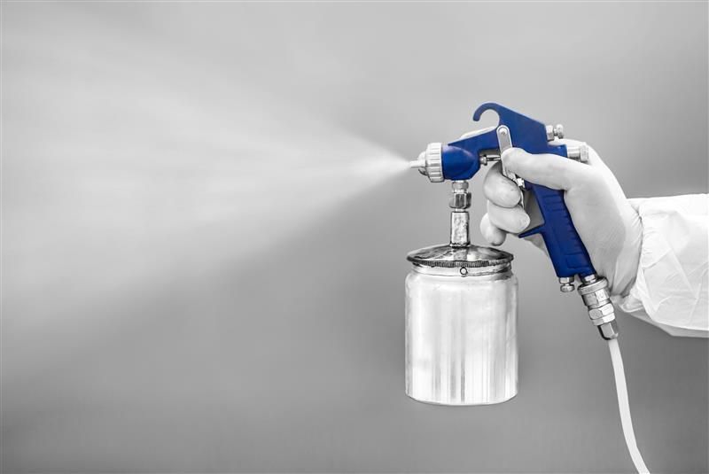 Person wearing gloves sprays blue paint with a spray gun on a gray wall.