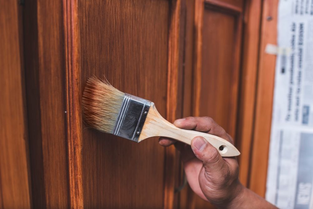 Person staining a wooden door with a paintbrush, brown color.