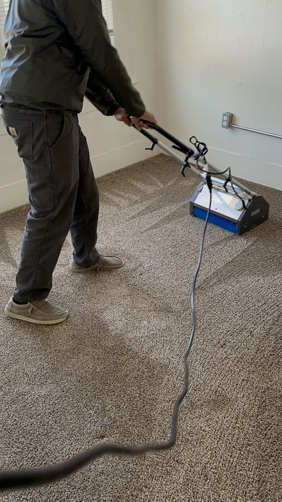 A man is using a vacuum cleaner to clean a carpet in a room.