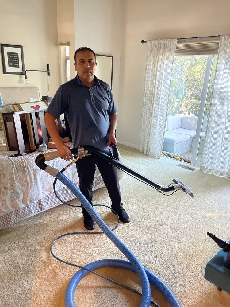 A man is standing in a bedroom holding a vacuum cleaner.