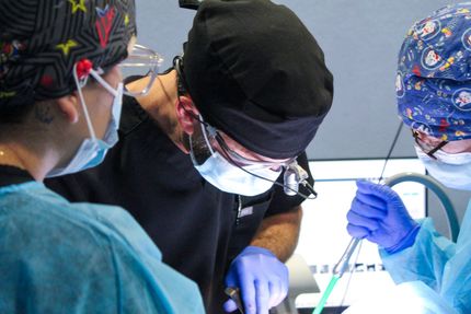 Surgeons in scrubs, masks, and caps operating in a sterile environment, focused on procedure.