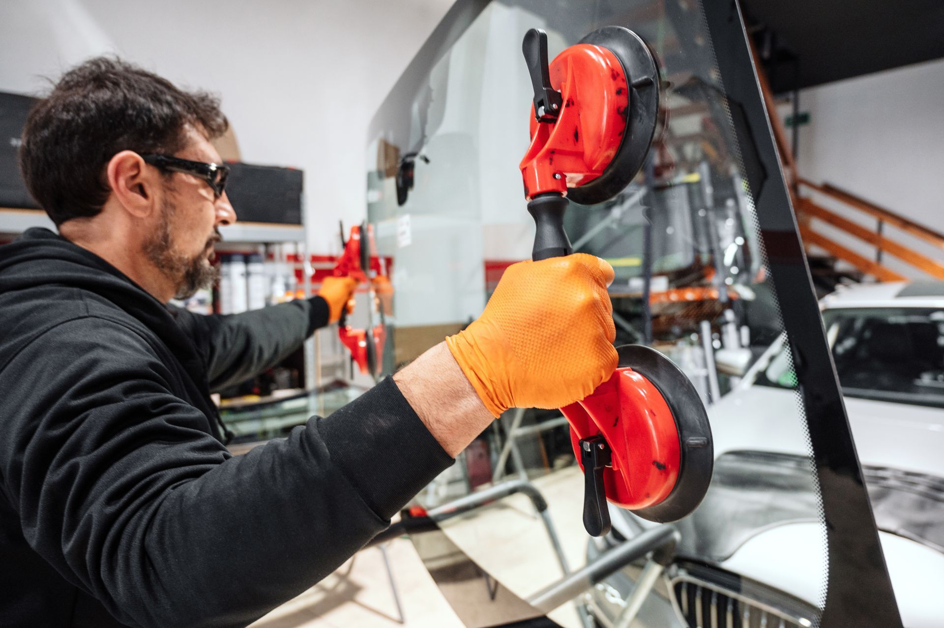 Man in orange gloves using suction cups to install a windshield in a garage.