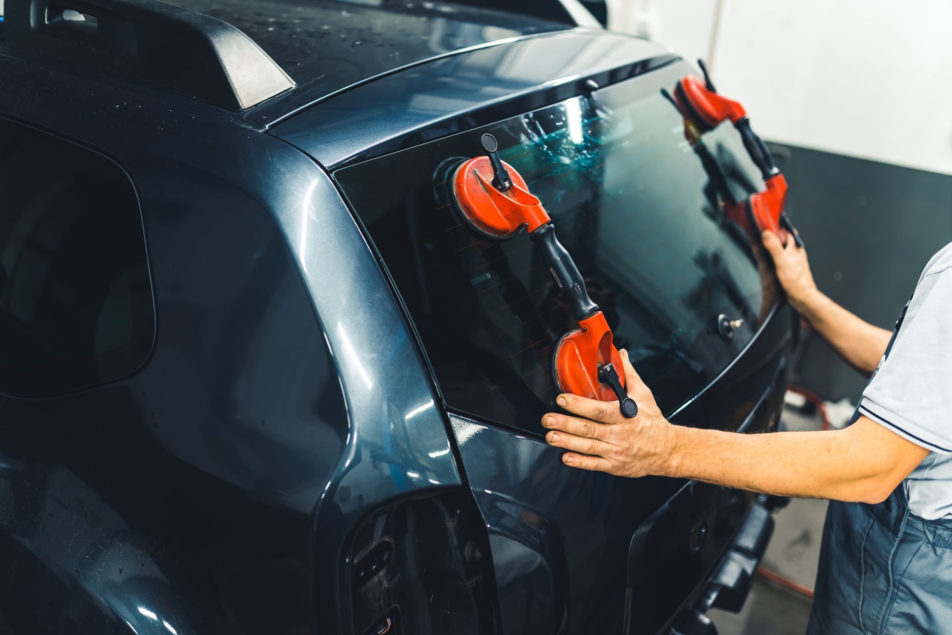 Person using suction cups to install a rear car window; in a garage.