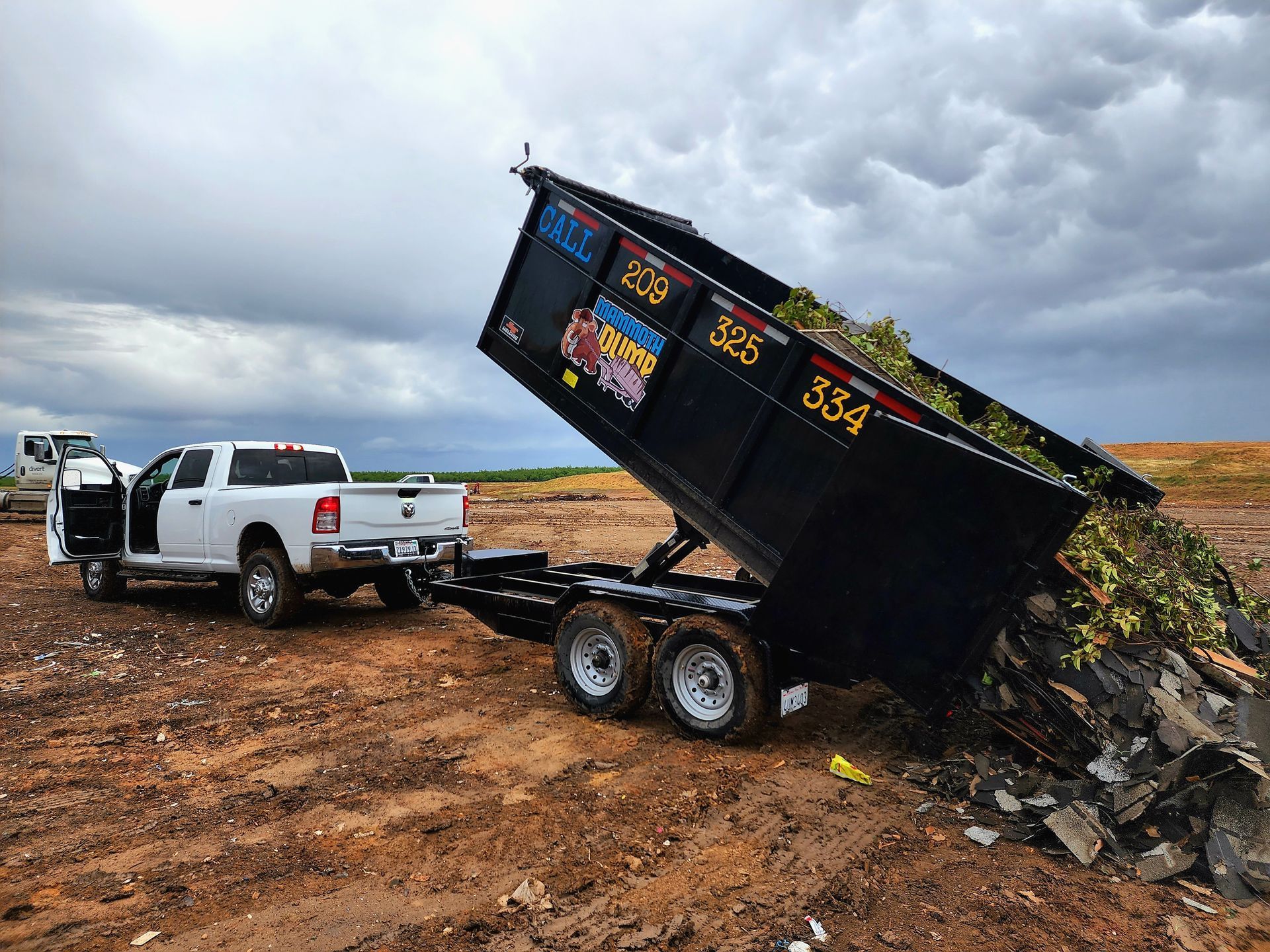 A 15-yard dumpster unloading roofing shingles and tree waste at a landfill, showing a mix of construction and organic debris.