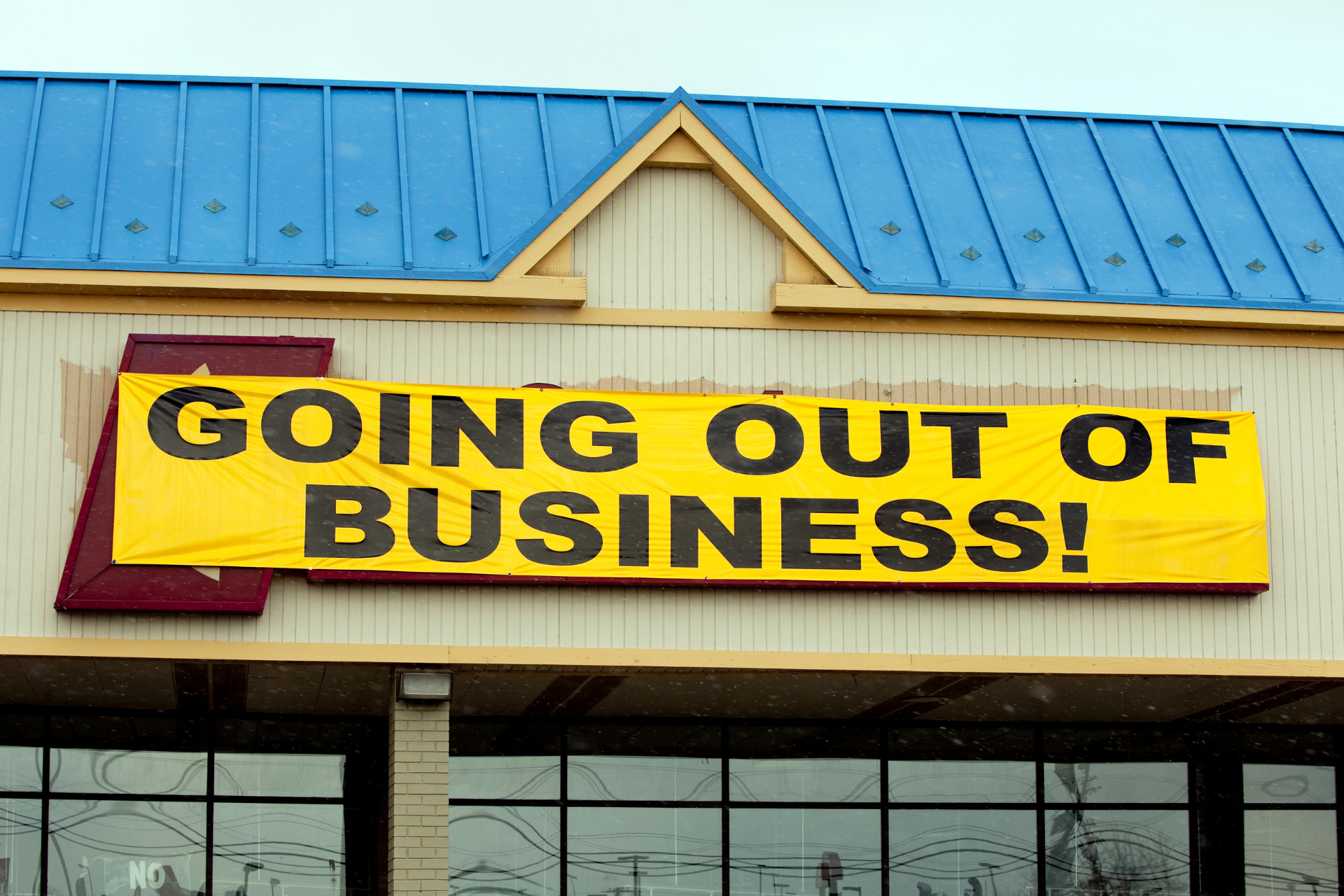 A commercial building storefront with a 'going out of business' sign prominently displayed over the store's original sign.