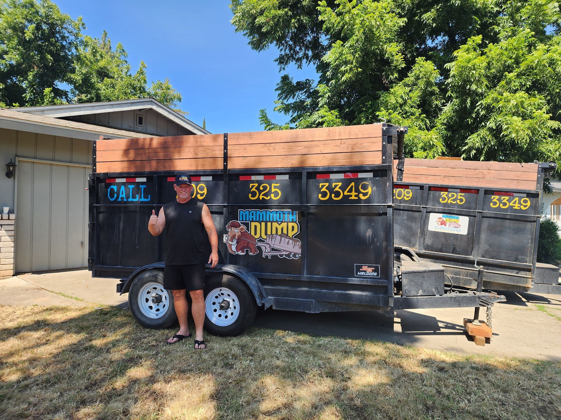 One of Mammoth Dump's satisfied customers standing in front of the 15-yard and 20-yard dumpsters he rented, holding a thumbs up and proudly wearing a Mammoth Dump hat.