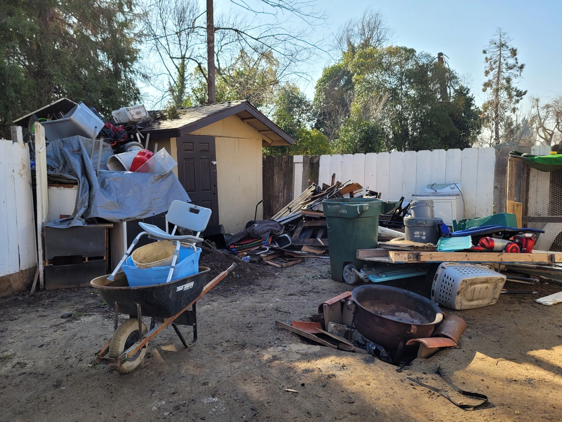 a pile of trash and junk that is as tall as the shed it is next to with various other items laid out in front of it