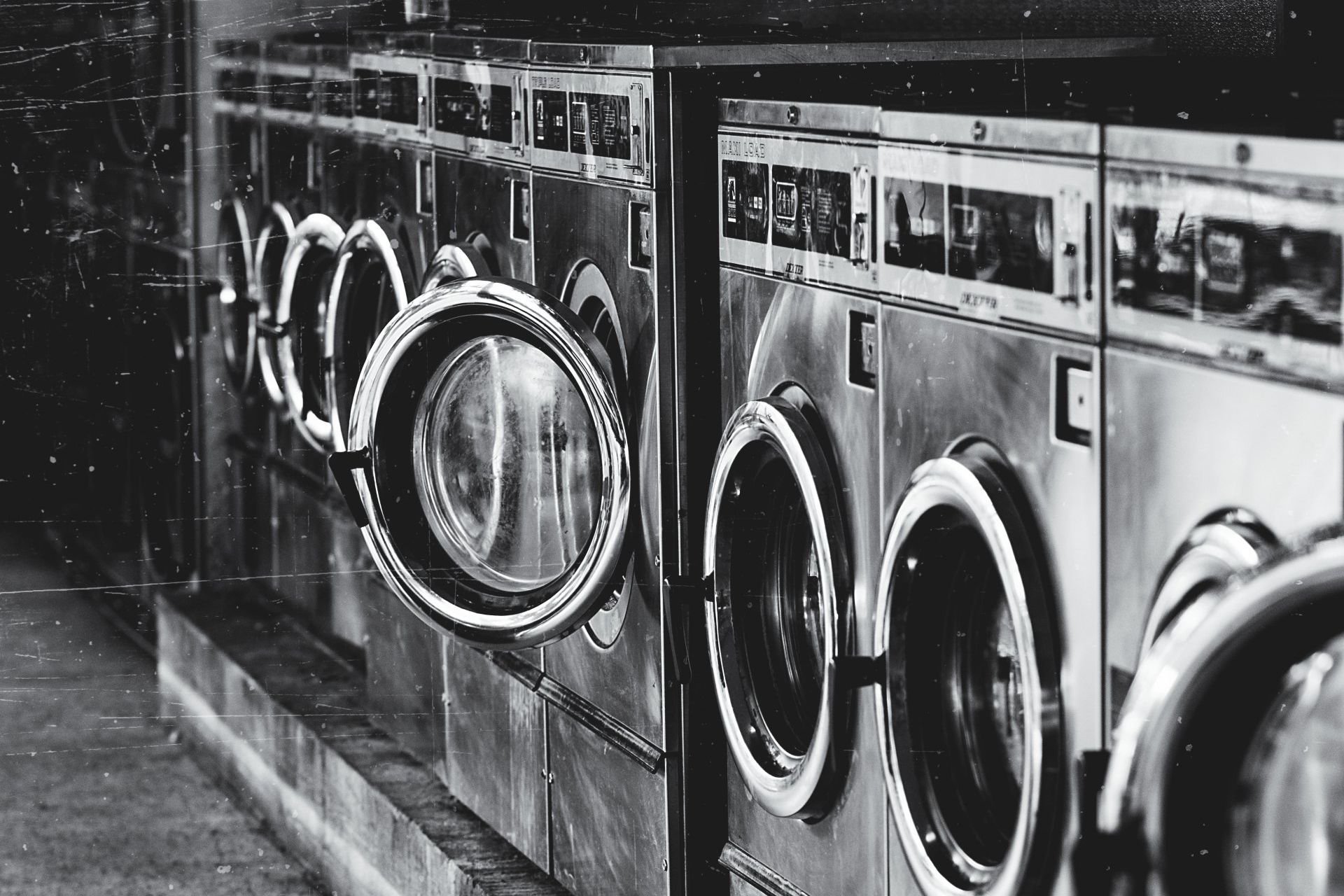 A black and white photo of a row of washing machines in a laundromat.