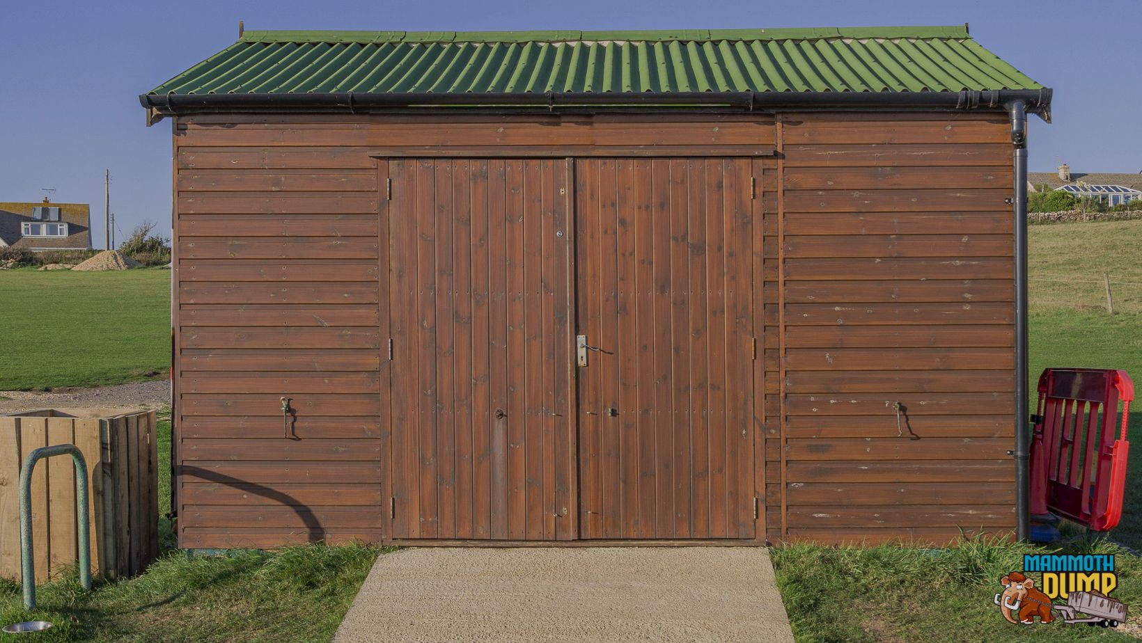 Brown shed with a green roof built out on an open field with paved pathway leading up to the doors
