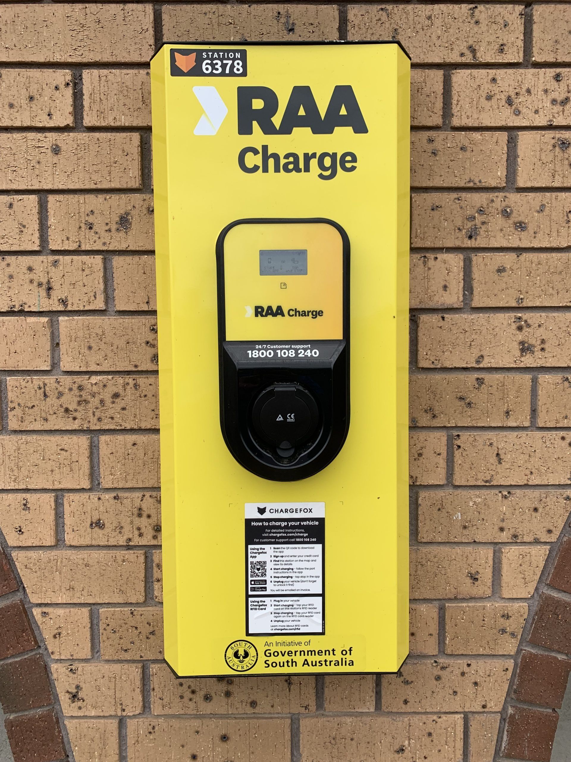 Yellow RAA Charge EV charger mounted on a brick wall