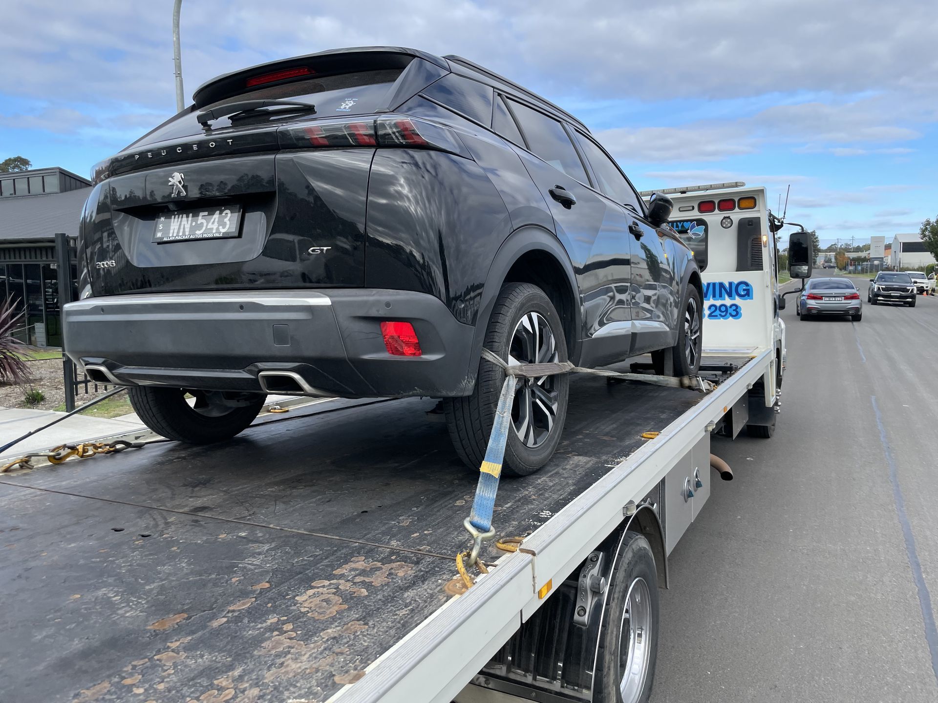 Black SUV being towed by a white tow truck on a paved road. Cloudy sky in the background. — M.L. Wray Towing & Automotive Repairs in Nowra, NSW