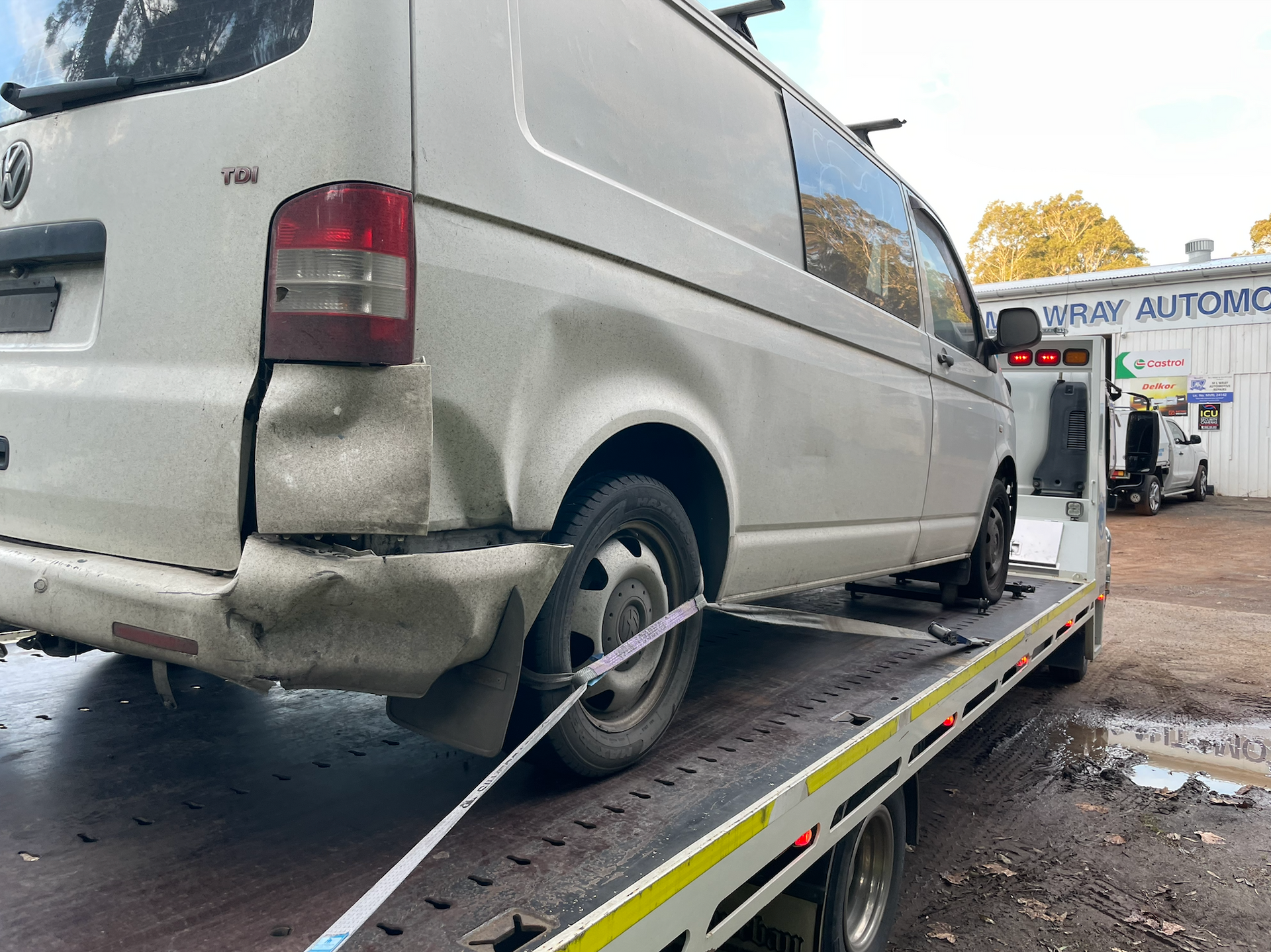 White van with rear damage loaded on a flatbed tow truck at a repair shop. — M.L. Wray Towing & Automotive Repairs in Nowra, NSW