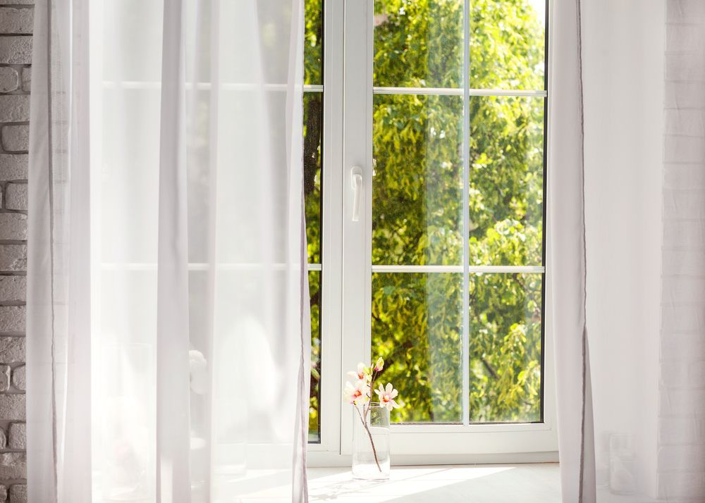 A window with white curtains and a vase of flowers on the window sill.