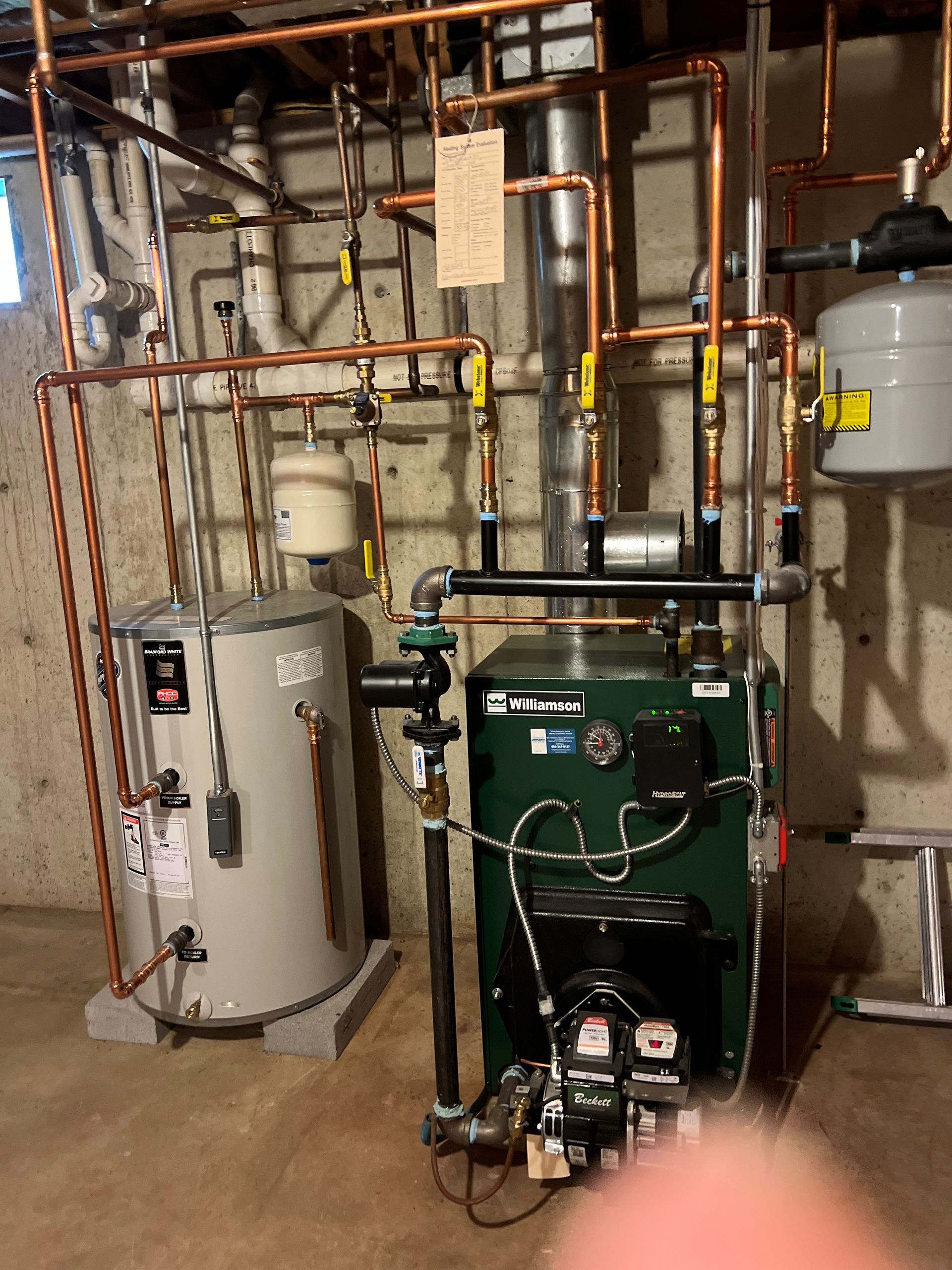 Plumbing and heating system with water heater, boiler, copper pipes, and expansion tank in a basement.