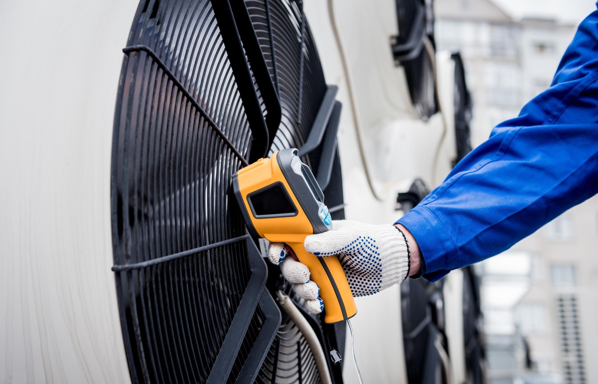 Person in blue jumpsuit uses a thermal scanner on an industrial fan.