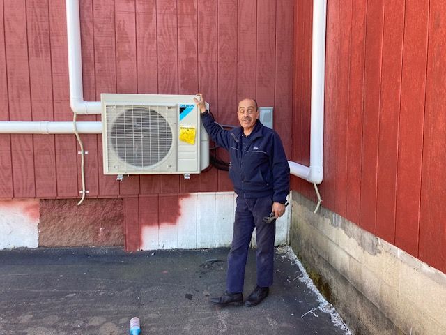 Man standing by an air conditioning unit on a red building exterior.