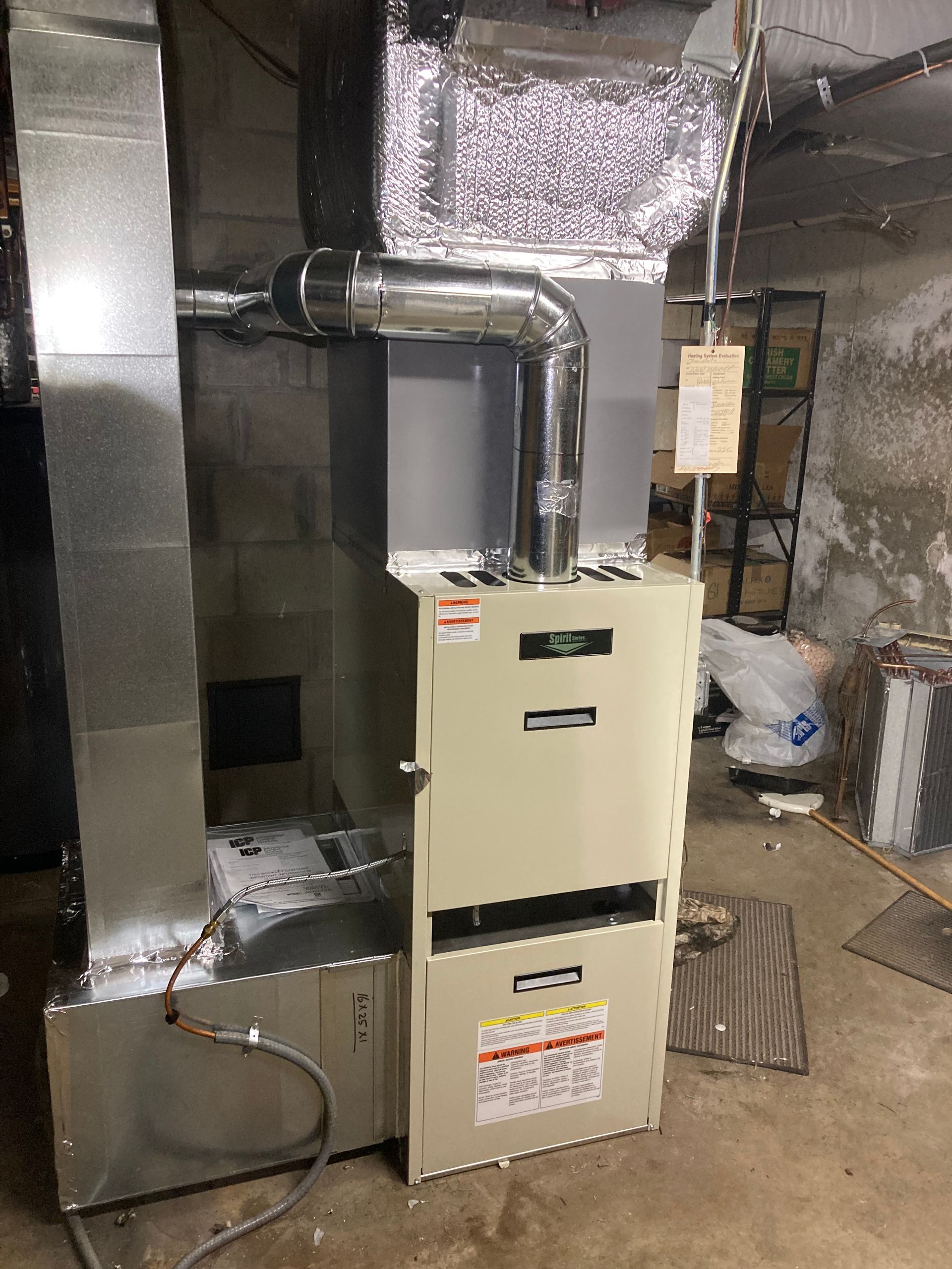 Furnace in basement with silver ductwork. Beige colored unit.