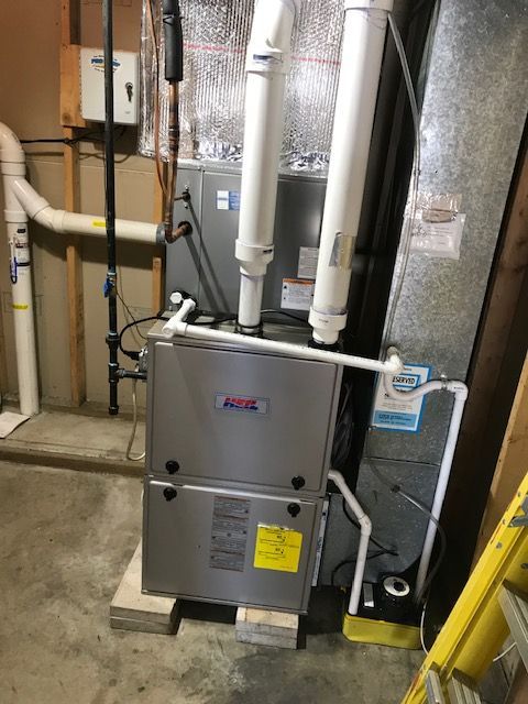 Furnace in a basement; silver metal unit with white pipes, sitting on wooden blocks.