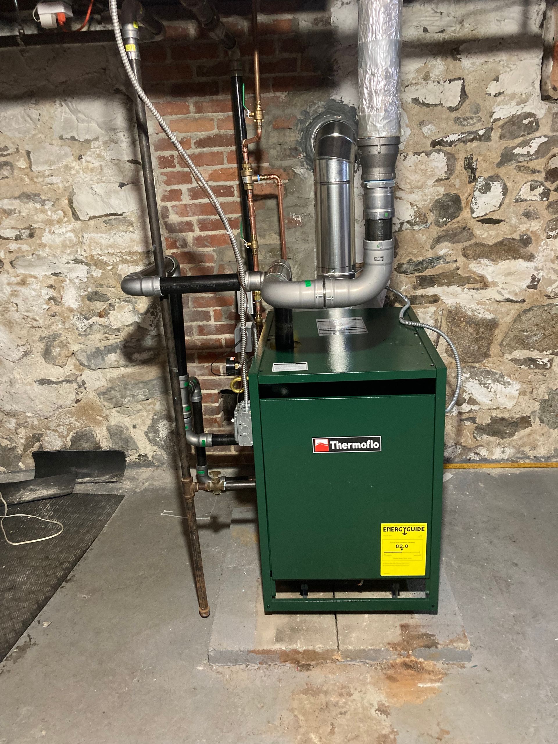 Green boiler unit in a basement, with brick and stone walls.