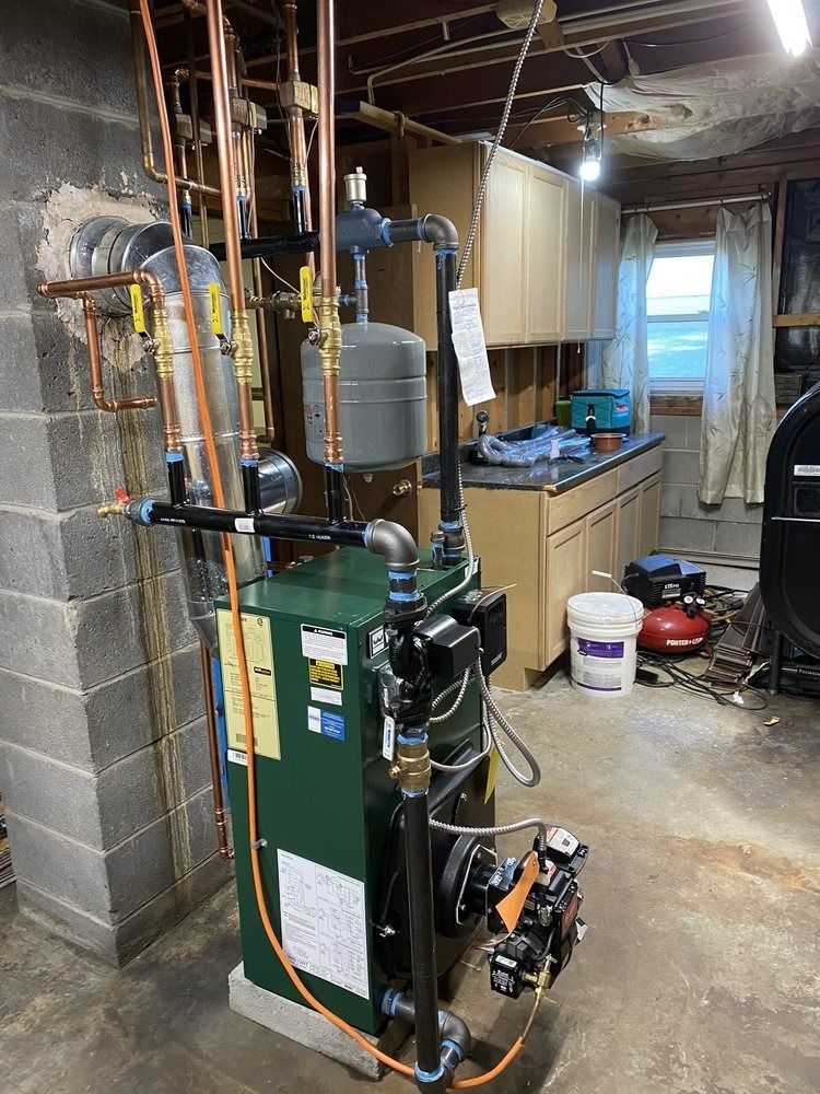 A residential heating system with copper pipes, a green boiler, and a gray expansion tank is in a basement setting.