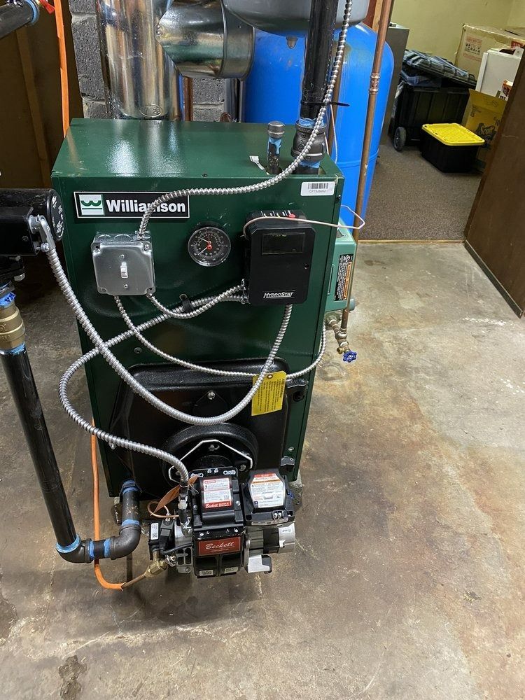 Green boiler with black pipes and controls in a utility room.