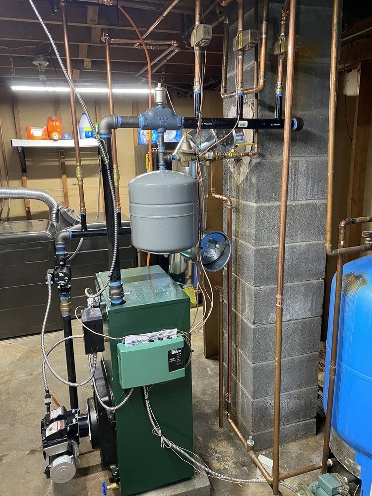 A boiler system with copper pipes, a gray expansion tank, and a blue water tank in a basement setting.