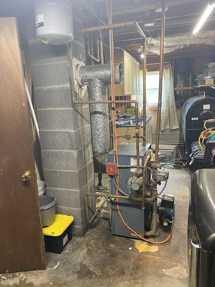 Furnace in a basement with copper pipes, vent, and water heater. Gray and copper tones.
