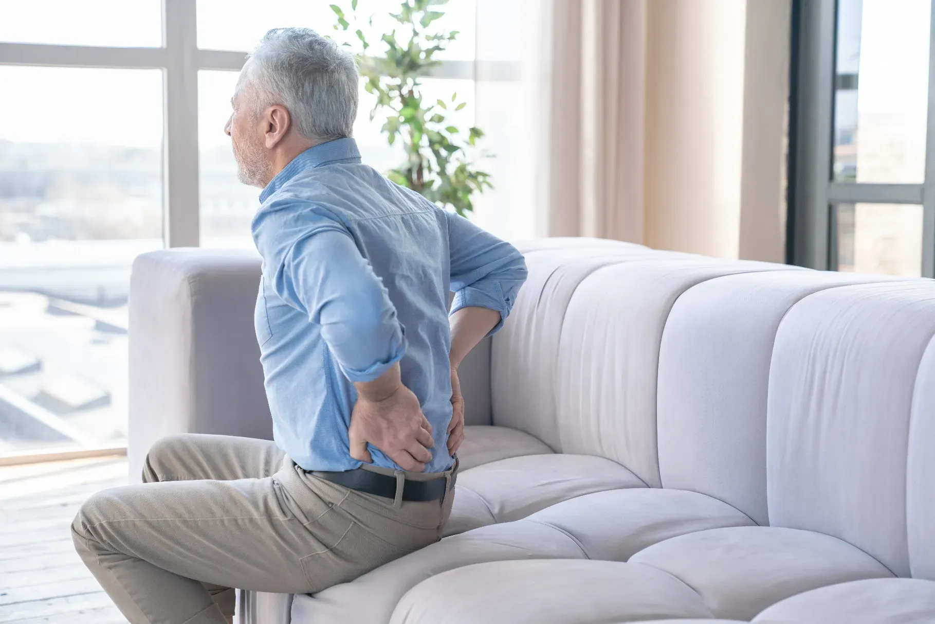 Man Seated on Sofa, Holding His Lower Back — Spinal Decompression Sunshine Coast In Buderim, QLD