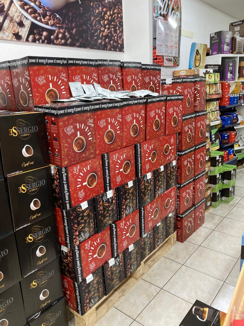 Pile di scatole di caffè rosse e nere esposte su un pallet di legno all'interno di un negozio al dettaglio.