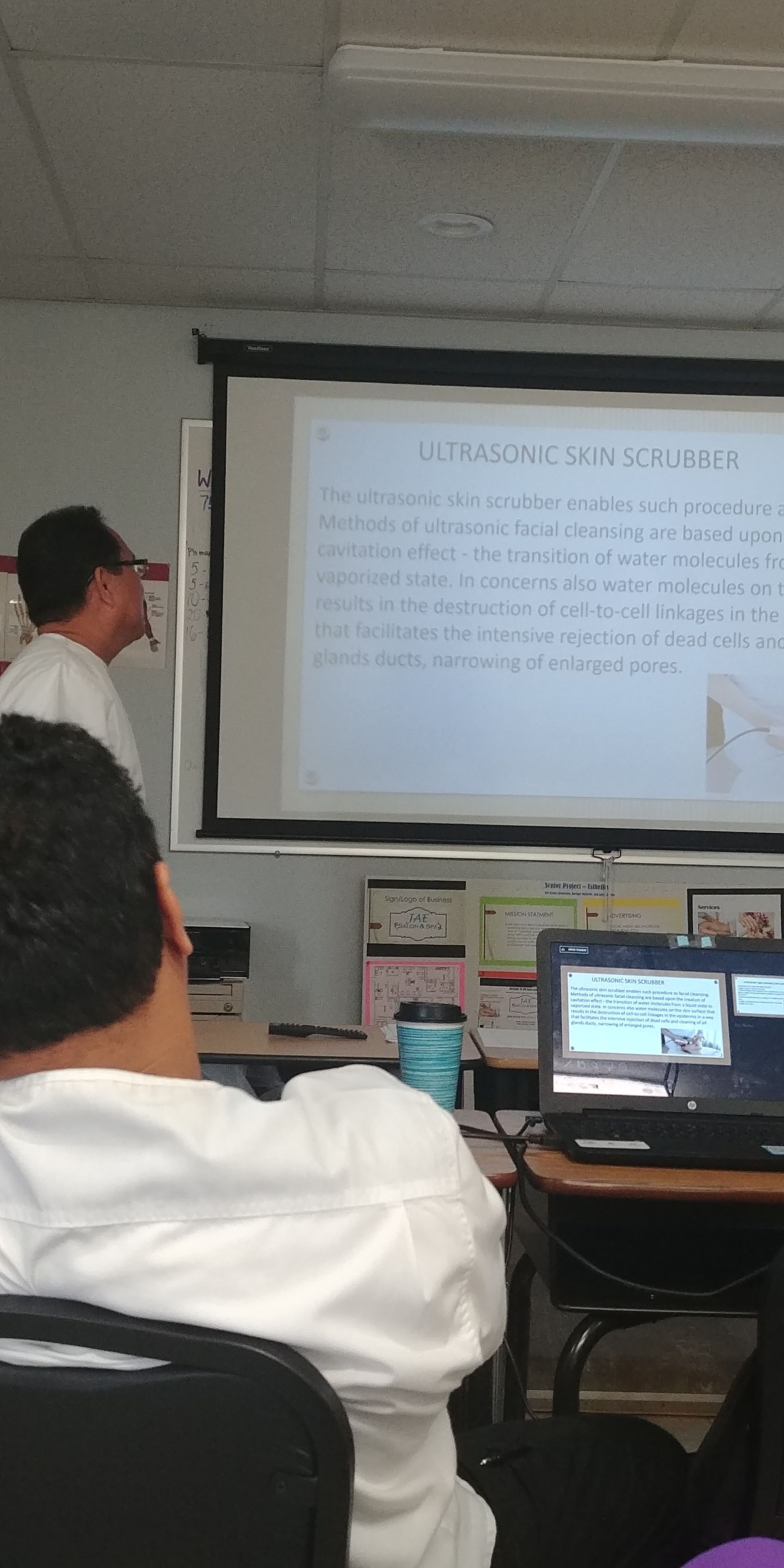 A man is giving a presentation in front of a projector screen in a classroom.