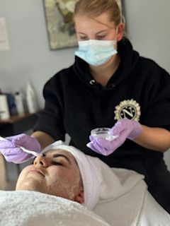 A woman wearing a mask and gloves is applying a cream to a woman 's face.