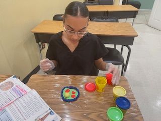 A woman is sitting at a desk playing with play dough.