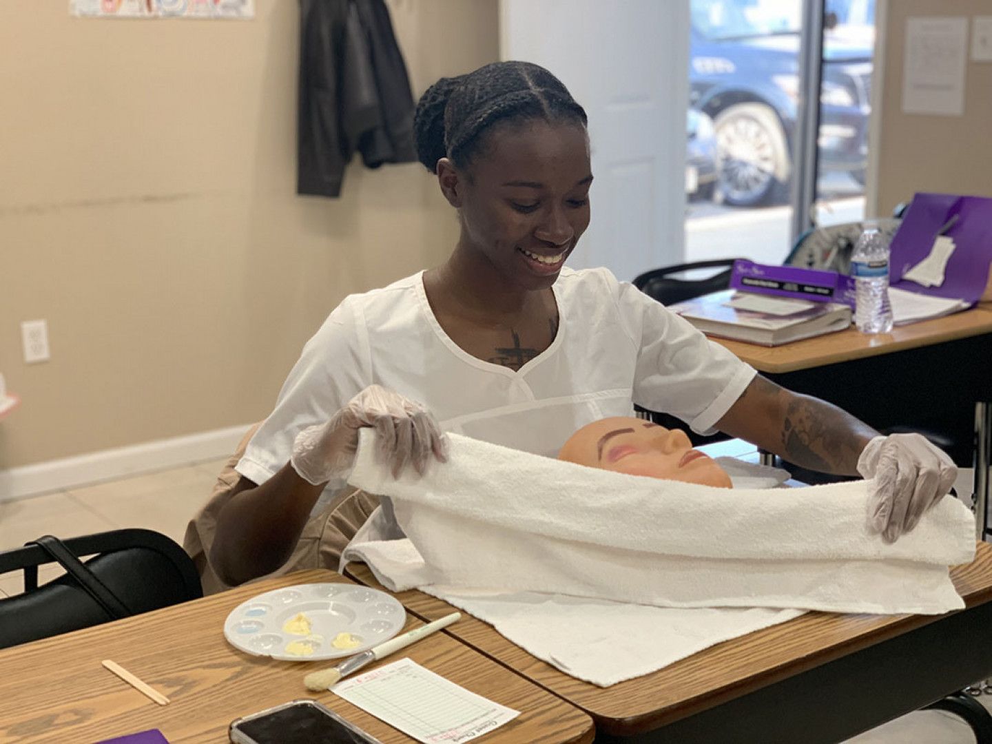 A woman is holding a towel over a mannequin 's face.