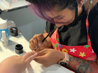 A woman in an apron is painting a person 's nails.