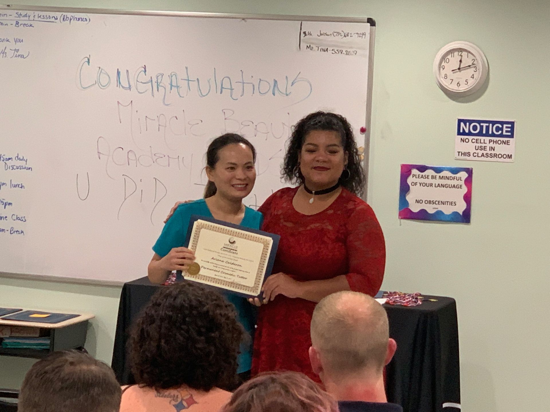 Two women are standing in front of a whiteboard holding a certificate.
